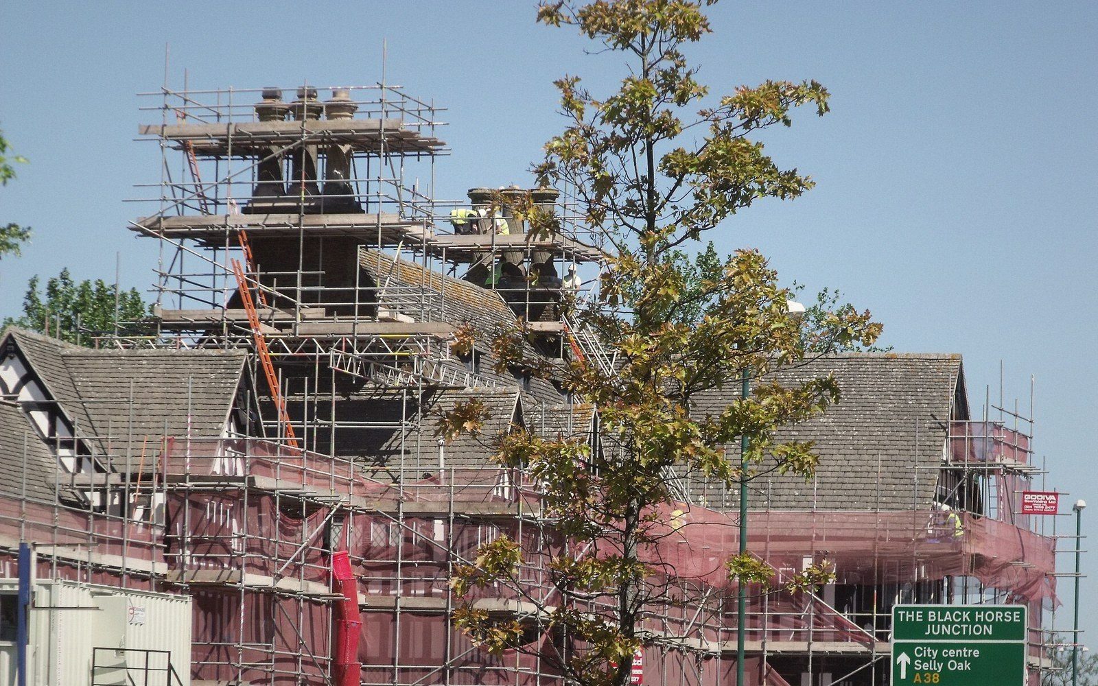 Scaffolding covers a mock-Tudor building's tiled roof and chimneys near the Black Horse Junction