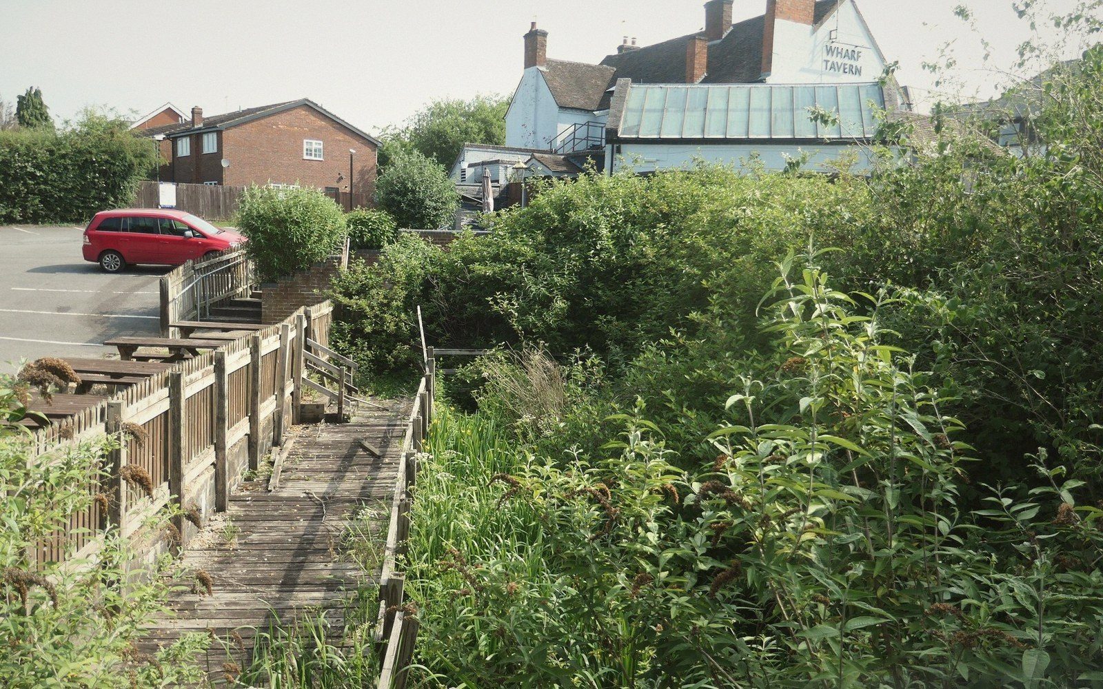 Wooden boardwalk beside overgrown vegetation leads towards the Wharf Tavern pub