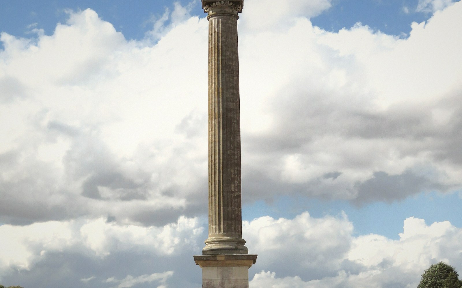 A tall stone column with a fluted shaft stands against a cloudy sky
