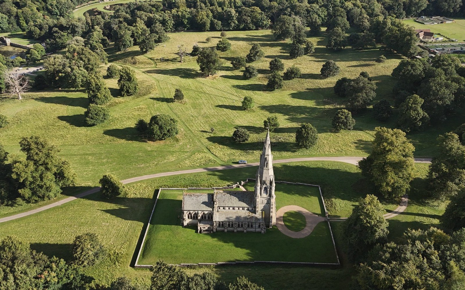 Aerial view of a spired church surrounded by parkland and mature trees on a country estate