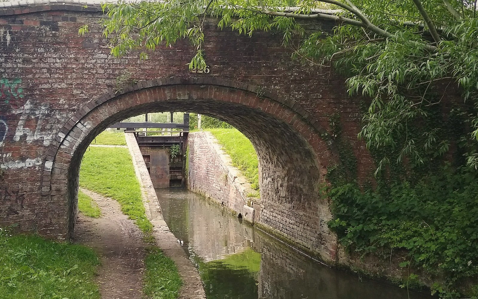 Brick arch bridge spans a narrow canal towpath leading to a lock gate