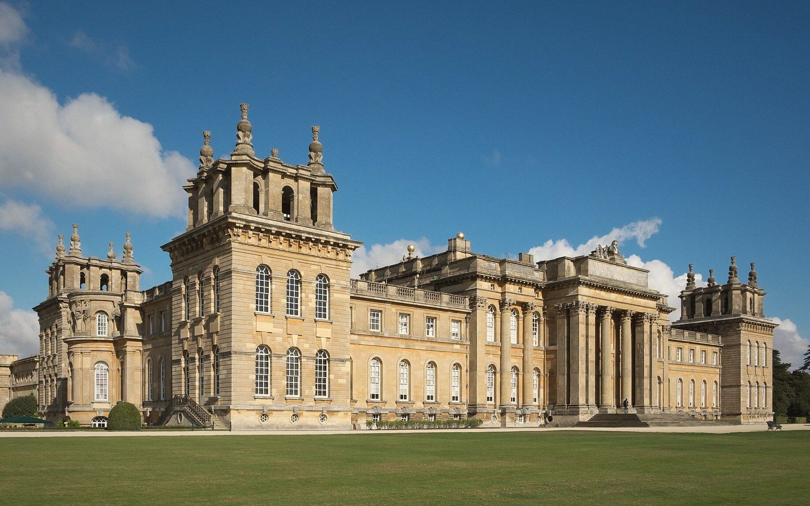 Baroque stone palace with columned facade and towers overlooking a wide lawn