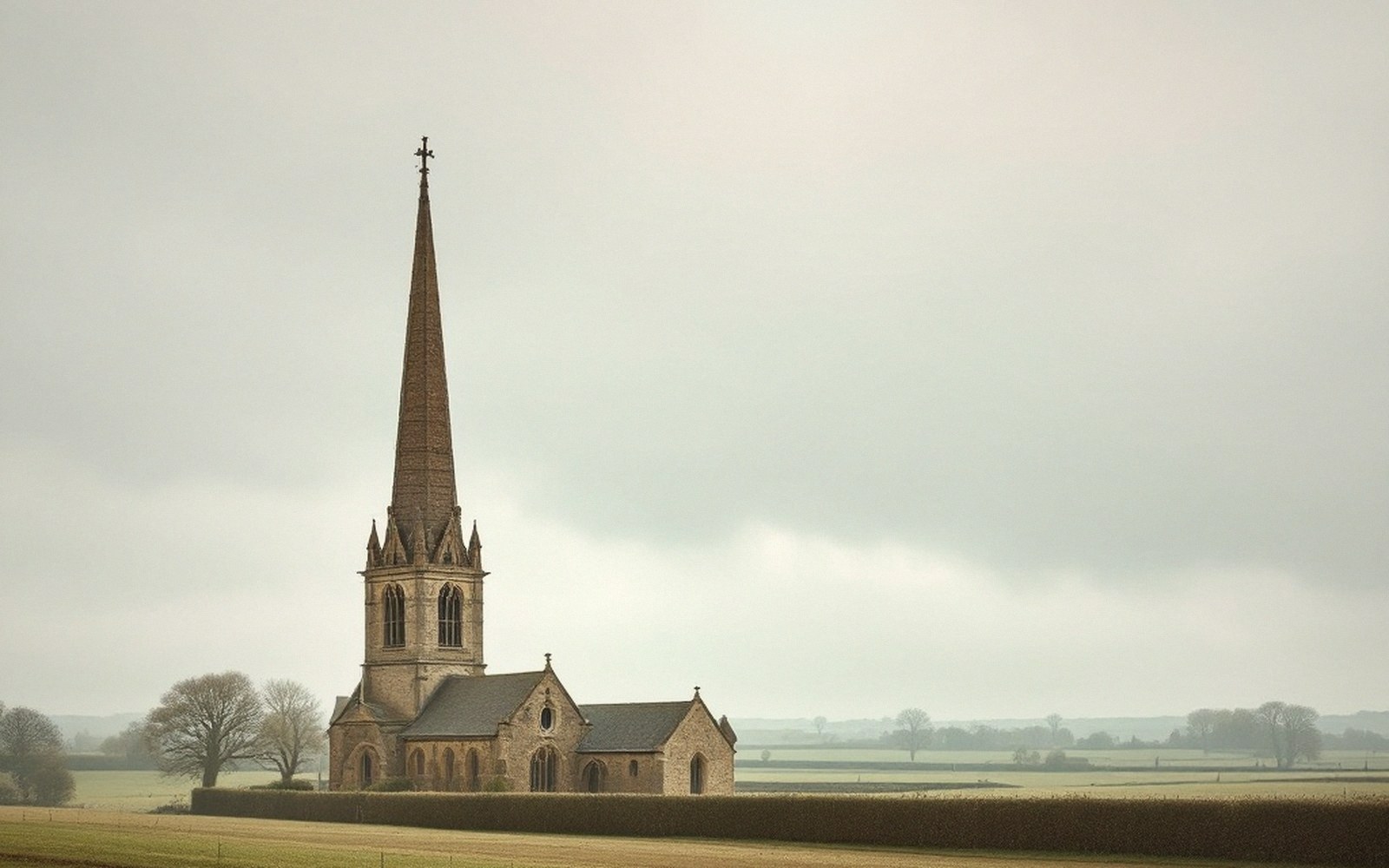 A church spire seen across open fields under a big ordinary sky